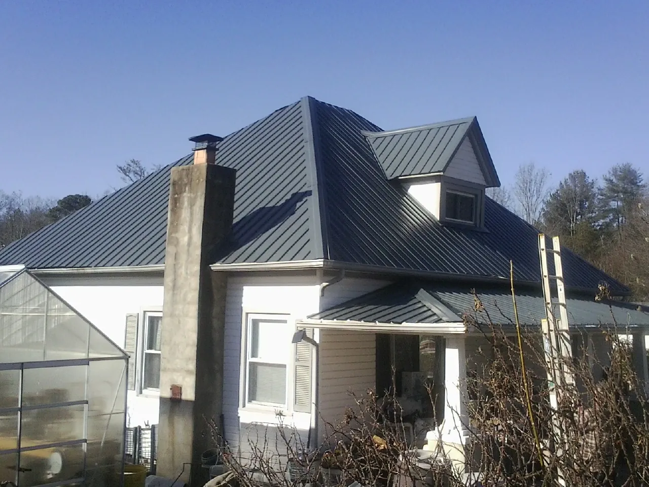 Dark blue standing seam metal roof on a white farmhouse with dormer — Slate & Tile Roof Repair by Roofing Brothers in Myersville