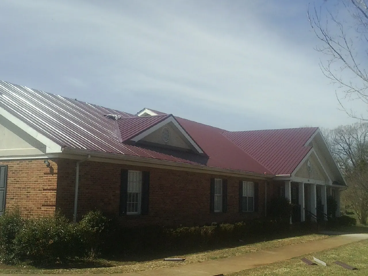 Red metal roof with gabled entries on a long brick building, from a Hail Damage Roof Repair job in Myersville