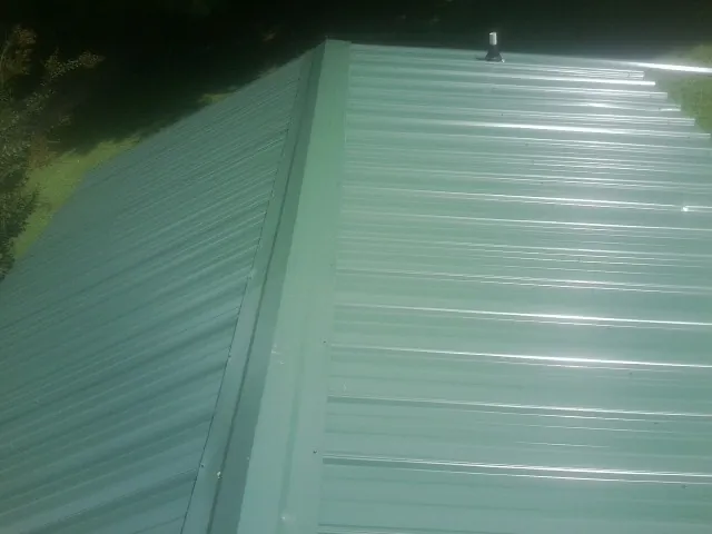 New green metal panels meeting at the ridge of a roof — Flat Roof Repair work by our crew in Myersville
