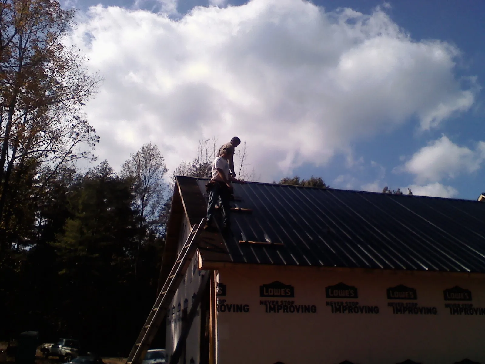 Roofer fastening dark metal panels high against a cloudy sky, from a Roof Inspection job in Myersville