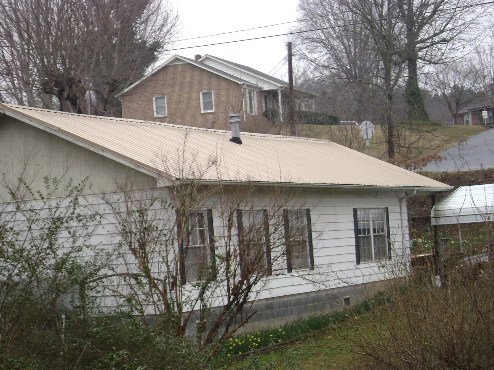 Tan metal roof on a white sided house set into a hillside — Commercial Roofing by Roofing Brothers in Myersville